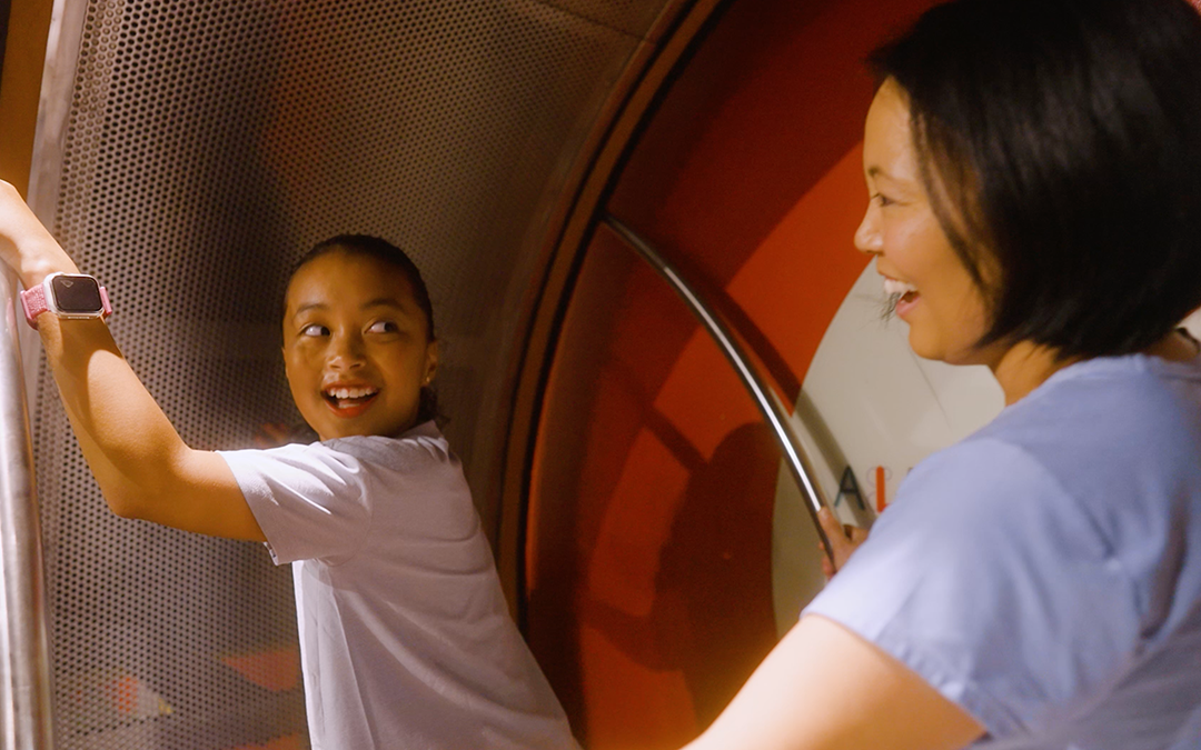 mother and daughter smiling at each other at Hands-On Museum in a giant wheel activity